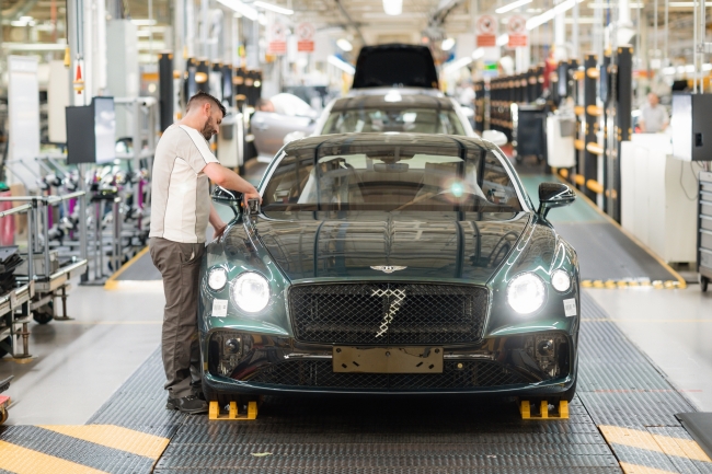 A man on the assembly line at the Bentley Motors factory in Crewe with an almost complete dark green car being tested ready to leave the factory