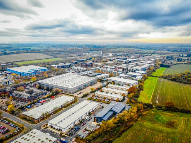 A high picture taken by a drone of a densely populated industrial area with lots of factory, warehouse and workshop units surrounded by fields and countryside